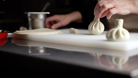 Chef carefully placing a single, raw khinkali dumpling onto a white cutting board, ready for cooking.の写真素材