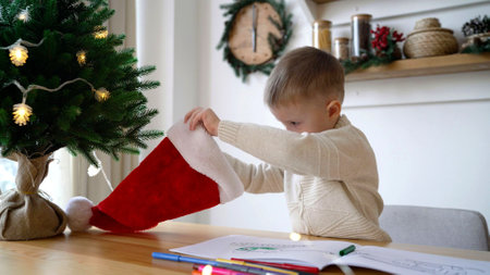 Curious boy looking for gifts in Christmas sock near xmas treeの写真素材