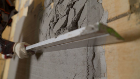 Construction worker using a spirit level while plastering a wall, ensuring a smooth and even surface.の写真素材