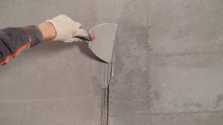 Construction worker is applying plaster on a wall using a spatula, during renovation works.