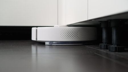 Smart robotic vacuum cleaner working on the floor in a modern apartment, cleaning under kitchen furnitureの写真素材