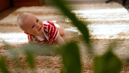 Happy baby wearing striped romper crawling on soft carpet at home, enjoying playtimeの写真素材
