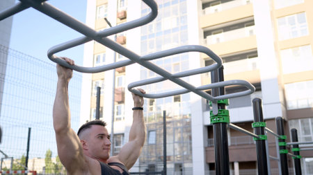 An athlete pulls himself up on a horizontal bar on a sports ground on the street. Young muscular man...