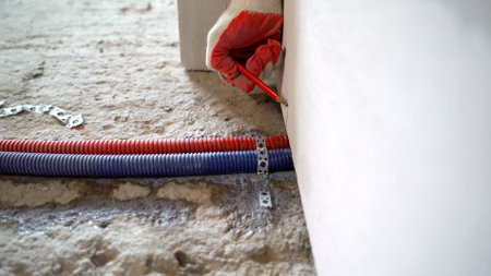 Construction worker marking wall using pencil near corrugated pipes during plumbing or electrical installation in building under constructionの写真素材