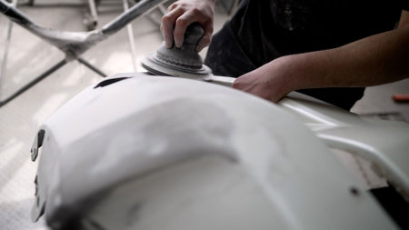 Car mechanic using a pneumatic polishing machine, smoothing a white car bumper in a professional...