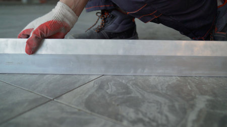 Professional contractor carefully installing precision aluminum threshold on sleek grey ceramic floor tiles during home renovation projectの写真素材