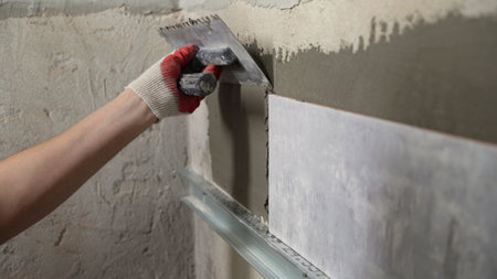 Construction worker applying cement glue with notched trowel on ceramic tiles during renovation...