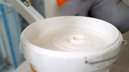 White paint being mixed in a bucket by a construction worker on a building site, creating swirling patternsの写真素材