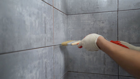 Construction worker waterproofing bathroom tiles using paint and brush during home renovation