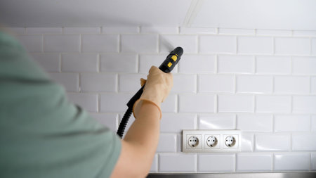 Cleaning lady wearing gloves operates a steam cleaner to effectively clean and sanitize white tiles in a kitchen environmentの写真素材