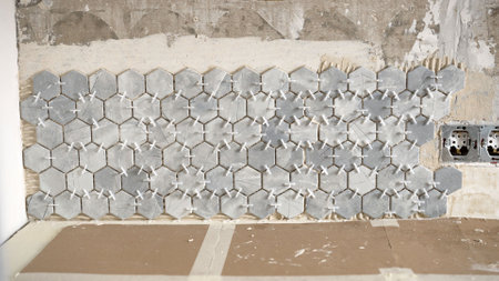 Close-up of hexagonal marble tiles being installed on a bathroom wall, showcasing the use of tile spacers for even grout linesの写真素材