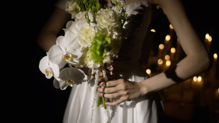 Fashion model wearing white wedding dress posing with bouquet in dimly lit room with many candlesの写真素材