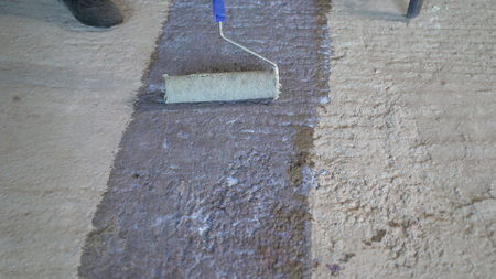 Construction worker uses paint roller to apply primer to concrete floor, preparing it for further...