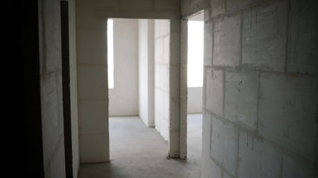 Interior of an unfinished apartment during construction, featuring exposed concrete block walls, doorways, and natural light illuminating the spaceの写真素材