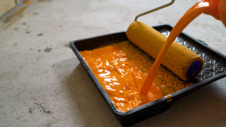 Pouring vibrant orange paint into a paint tray, preparing for an exciting painting project with a roller, enhancing home interiorsの写真素材