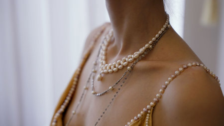 Clothing and accessories of the 20th century. Woman wearing layered pearl necklaces draped elegantly over soft gold dress, showcasing luxurious fashion accessories with refined sophisticationの写真素材