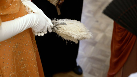 Elegant woman in vintage-inspired orange dress and white gloves delicately holding ornate feather...