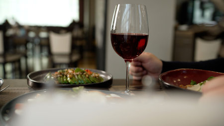 Glass of red wine sits on restaurant table near plates of fresh salad, creating an elegant dining atmosphereの写真素材