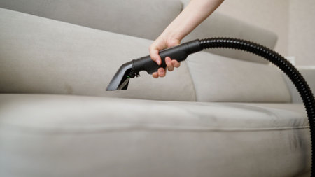 Professional cleaning service worker removing stubborn stains from a sofa, expertly using a vacuum cleaner for effective upholstery cleaningの写真素材