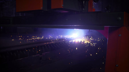 Precision laser cutting through metal sheet, generating intense sparks and luminous glow within dark...