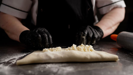 Professional baker wearing black gloves carefully folding traditional Georgian khachapuri dough on gleaming metal kitchen workspaceの写真素材