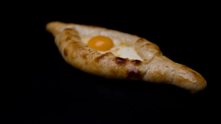 Adjara khachapuri, a traditional Georgian dish, rotates slowly against a dark backdrop, showcasing its golden crust and single eggの写真素材