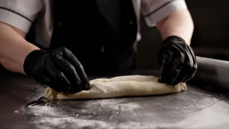 Professional chef working with rolling pin, flattening pizza dough on stainless steel surface in commercial kitchen, showcasing culinary expertise and precise food preparation techniqueの写真素材