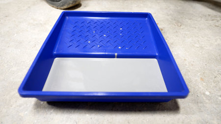 Blue paint tray containing white paint sits on a concrete floor, ready for use in a home renovation...