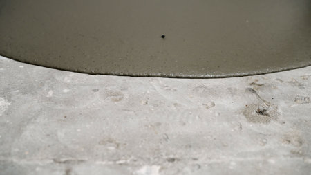 Professional contractor smoothing self-leveling concrete, creating seamless, even floor surface during industrial renovation process with grey viscous material spreading evenlyの写真素材