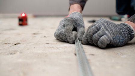 Close-up of hands in gloves meticulously placing yellow clips on a metal profile, preparing for precise floor tile installationの写真素材