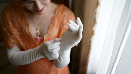 Elegant woman wearing a flapper dress putting on long white gloves, getting ready for a special occasionの写真素材