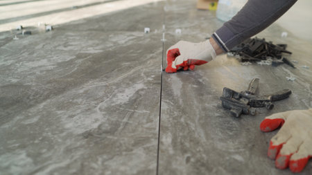 Close-up of a tiler's hands inserting tile spacers between ceramic tiles during a floor renovationの写真素材