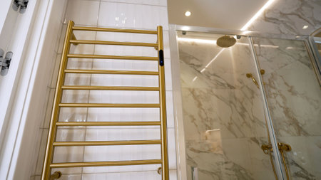 Modern bathroom interior with golden towel warmer and shower cabin with marble tiles, creating a luxurious and elegant atmosphereの写真素材