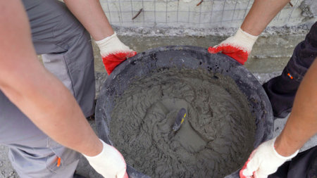 Construction workers holding a bucket filled with cement mix, ready to be used on a building siteの写真素材