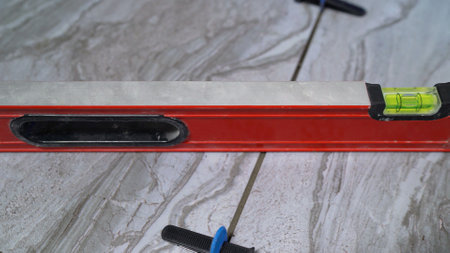 Red spirit level placed on ceramic tile during renovation work, ensuring precise alignment and a...