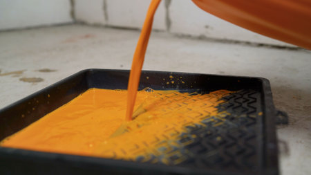 Orange paint is being poured into a black paint tray, preparing for a home repair or painting projectの写真素材