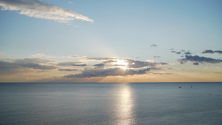 Sun shining through clouds over calm ocean at sunsetの写真素材