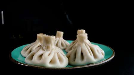 Steaming hot khinkali dumplings resting on teal plate, black background