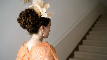 Elegant woman wearing feather headdress and vintage dress standing next to staircaseの写真素材