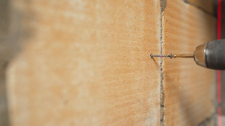 Close-up of cordless screwdriver driving screw into wall, demonstrating construction and renovation...