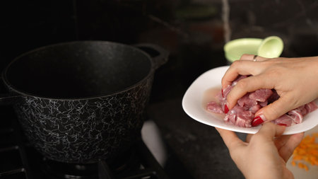 Female chef preparing pork meat for cooking, adding pieces of raw pork meat into a pot in the kitchenの写真素材