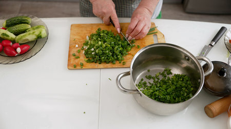Green onions getting chopped on wooden cutting board, freshly diced scallions falling into stainless...