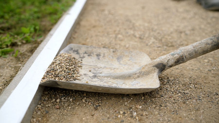 Construction worker uses shovel to spread gravel evenly along a concrete border, creating a neat and...