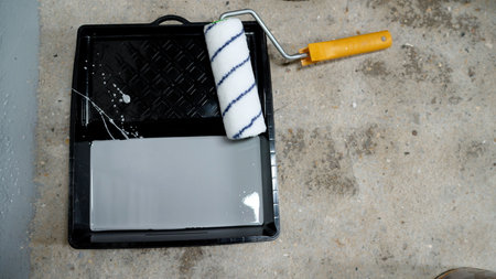 Paint roller and tray filled with gray paint resting on a concrete floor, preparing for an exciting...