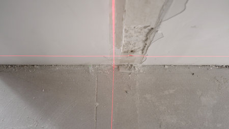 Close-up shot of a professional builder's hand marking a plasterboard ceiling. The worker uses a pencil and a laser level for precisionの写真素材