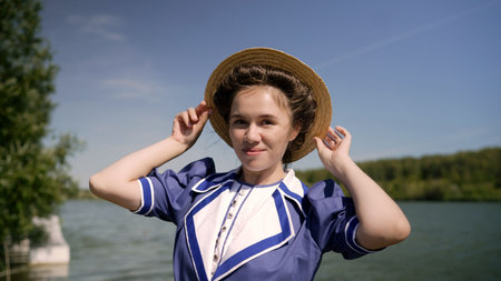Elegant woman adjusting straw hat by the lakeの写真素材