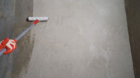 Construction worker applying a coat of primer to a concrete wall using a paint roller, preparing it...