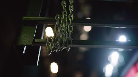 Metal chain hanging on an industrial structure. Defocused bokeh lights creating a modern abstract background in a dark settingの写真素材