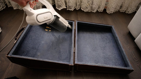 Man using a modern handheld vacuum cleaner to remove dust and crumbs from the inside of an old, dusty vintage suitcase with blue liningの写真素材