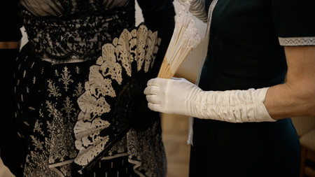Two women wearing elegant historical dresses and white gloves holding vintage lace hand fans. Historical reconstruction of Victorian era fashion and accessoriesの写真素材